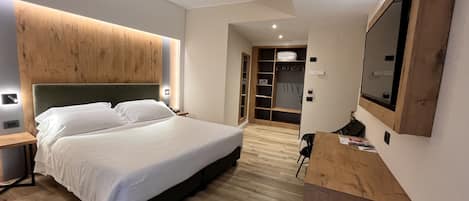 Quarto moderno com cama grande, cabeceira de madeira, guarda-roupa embutido e televisão de tela plana presa à parede.