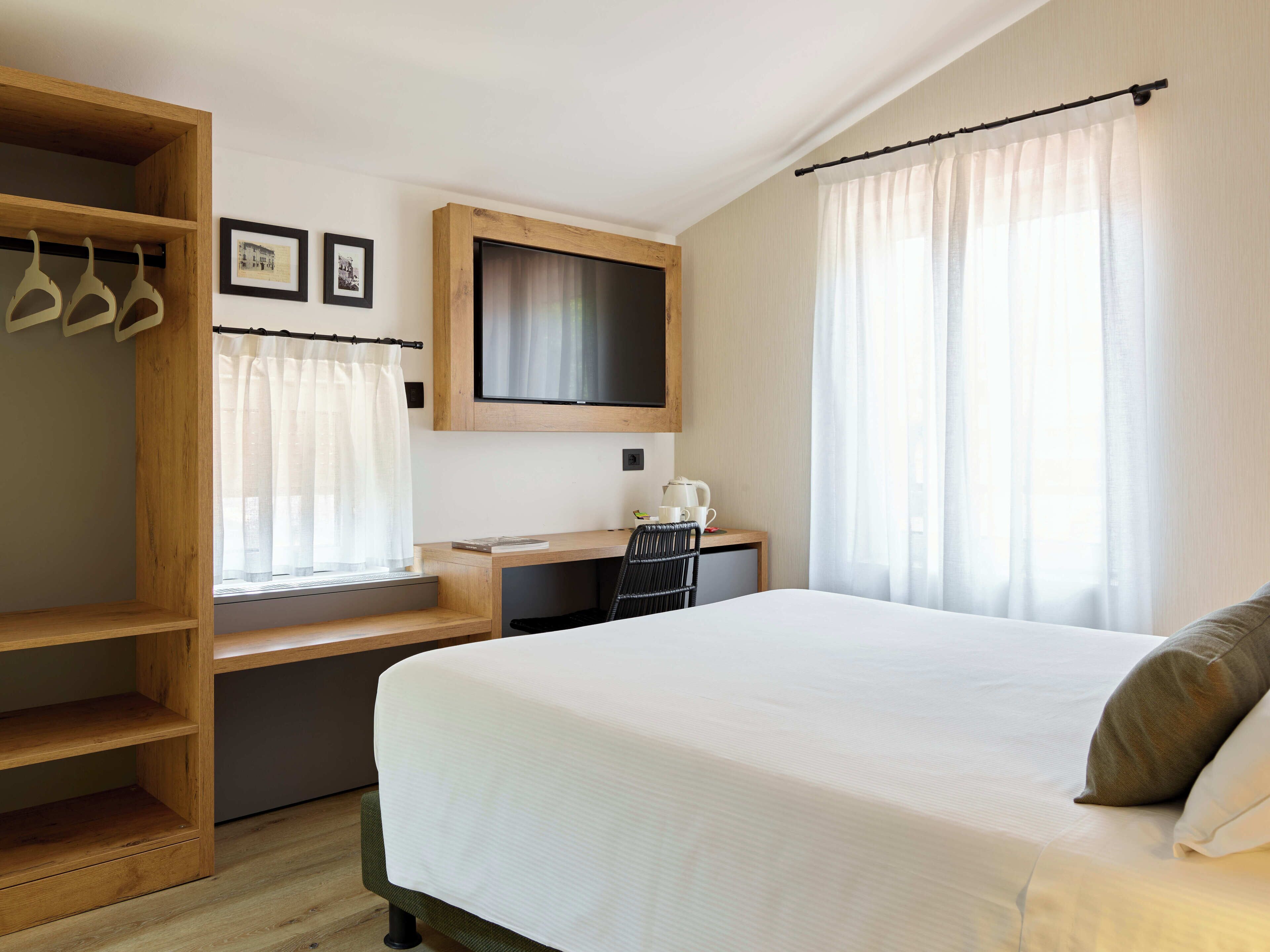 Una habitación de hotel con cama, escritorio, televisor y armario.