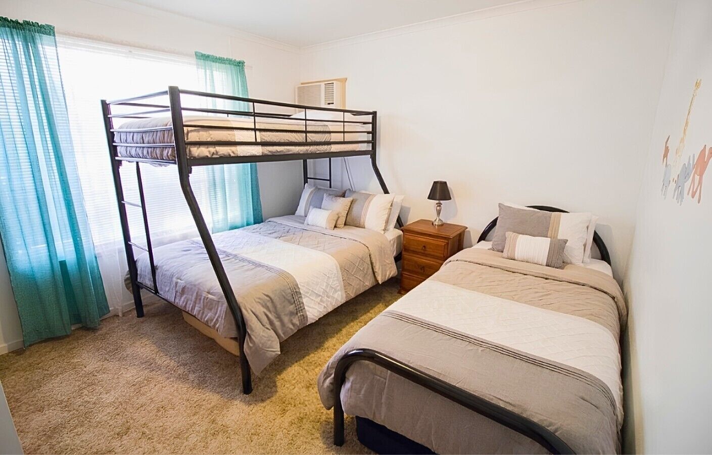 A room with two bunk beds, a bedside table with a lamp, and a window with curtains.
