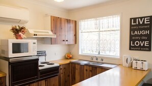 Eine moderne Küche mit Mikrowelle, Herd, Spüle und Toaster. Ein Fenster mit Spitzenvorhängen und ein motivierendes Zitat an der Wand.