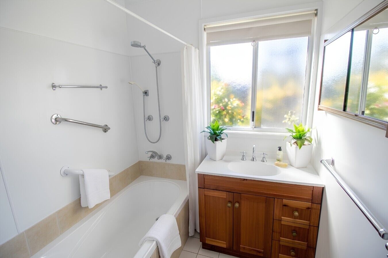 A bathroom with a bathtub, shower, vanity with a sink, and a window with a view.