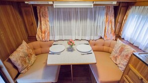 Interior acolhedor de uma casa móvel, com mesa de jantar, assentos estofados e cortinas.