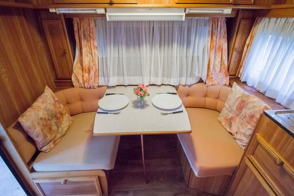 A cozy RV interior with a dining table, cushioned seating, and curtains.