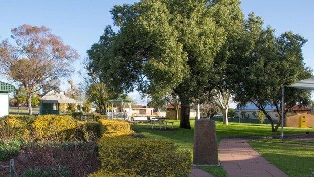 Um parque com um coreto, uma mesa de piquenique e um monumento de pedra.