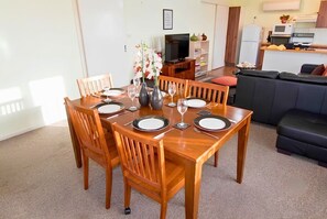 A dining area with a wooden table set for four, a sofa, and a kitchenette in the background. - Charming Pet-Friendly Cottage & Caravan | Sleeps 8 (Manilla)