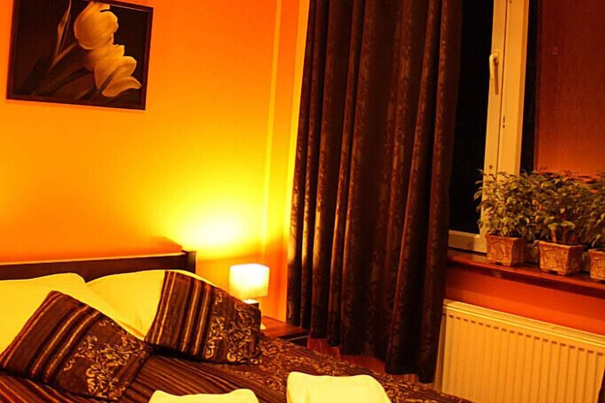 Hotellihuone, jossa on sänky, ikkuna verhoilla, patteri ja seinälle ripustettu taulu.