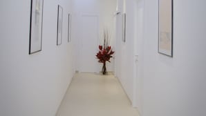 A modern hallway with white walls, framed artwork, and a central plant. - Castellani a San Pietro (Rome)