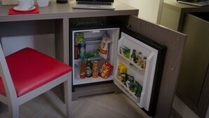 A compact kitchenette with a refrigerator stocked with beverages and snacks, a small table with a laptop, and a red chair. - Castellani a San Pietro (Rome)