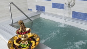 Una bañera con caída de agua, un frutero con diversas frutas y una escalera metálica.
