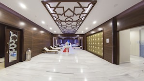 Un moderno vestíbulo de hotel con piso de mármol, sillones de descanso, una fuente central y un techo decorativo.