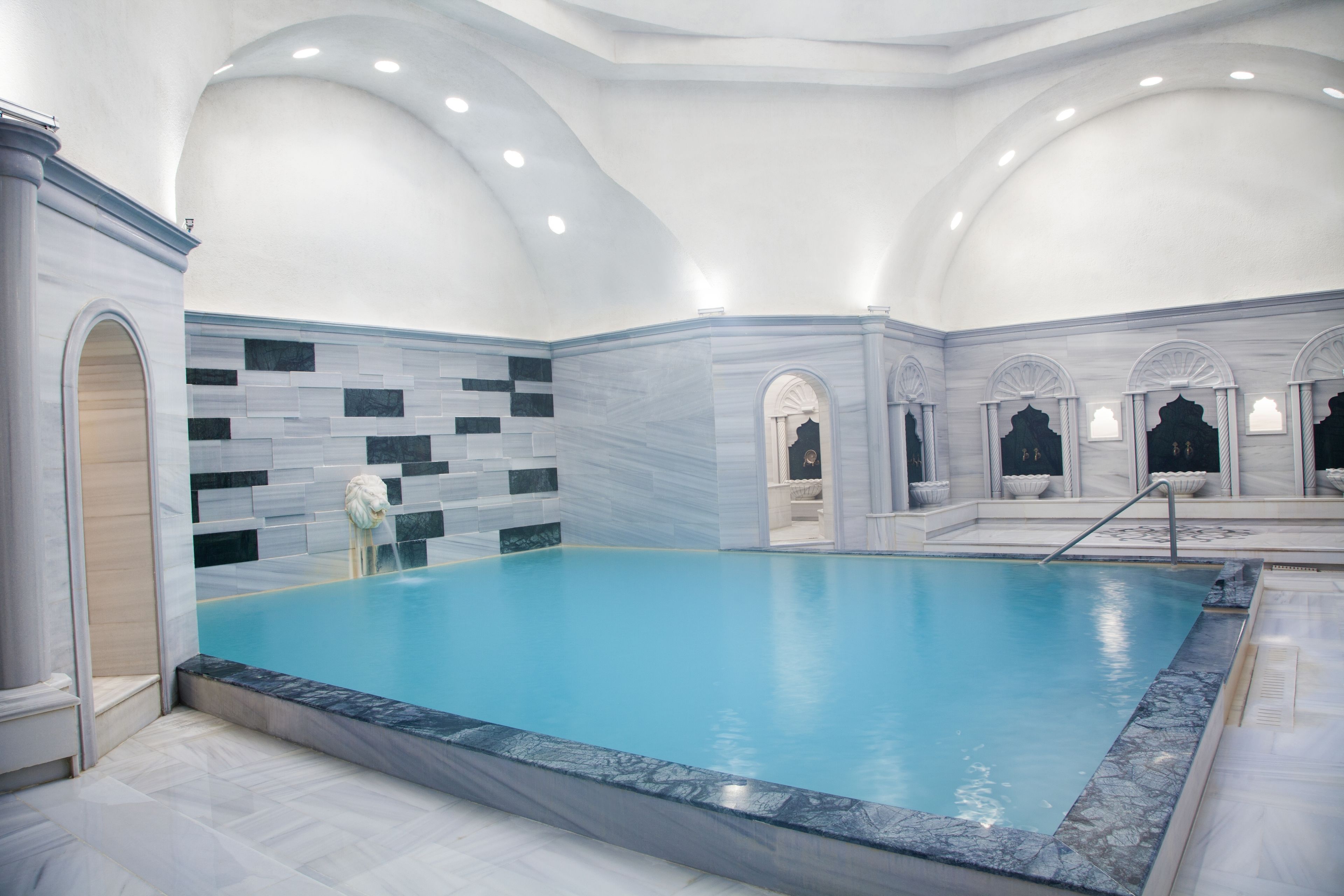 A large indoor swimming pool with a marble border and a tiled wall.