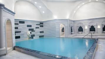 A large indoor swimming pool with a marble border and a tiled wall.
