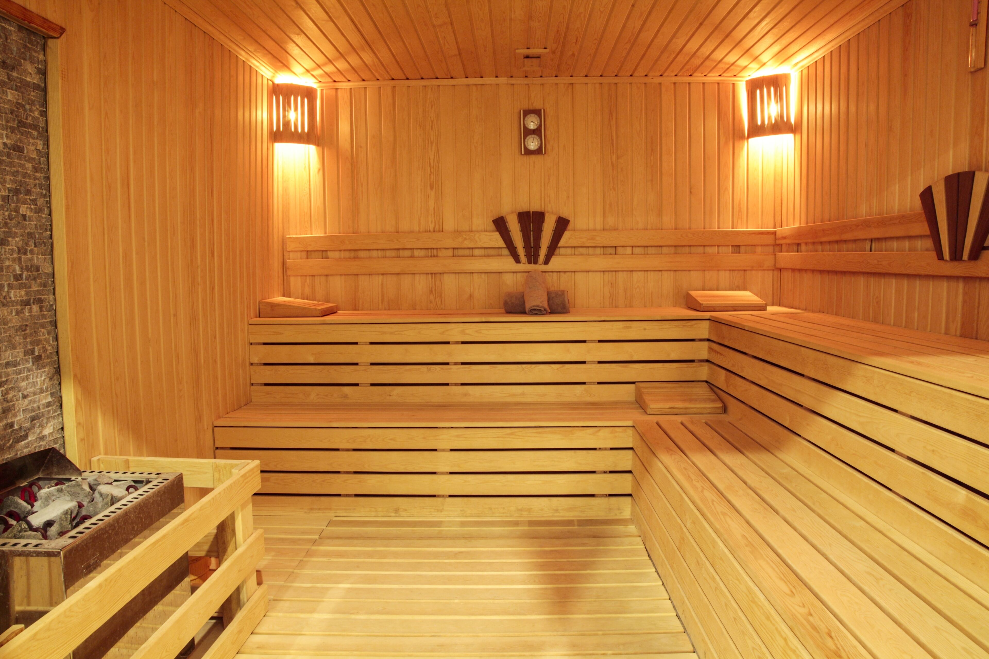 Eine Sauna mit Holzbänken, die in einer Halbkreisform angeordnet sind, einer Uhr an der Wand und zwei Wandleuchten.