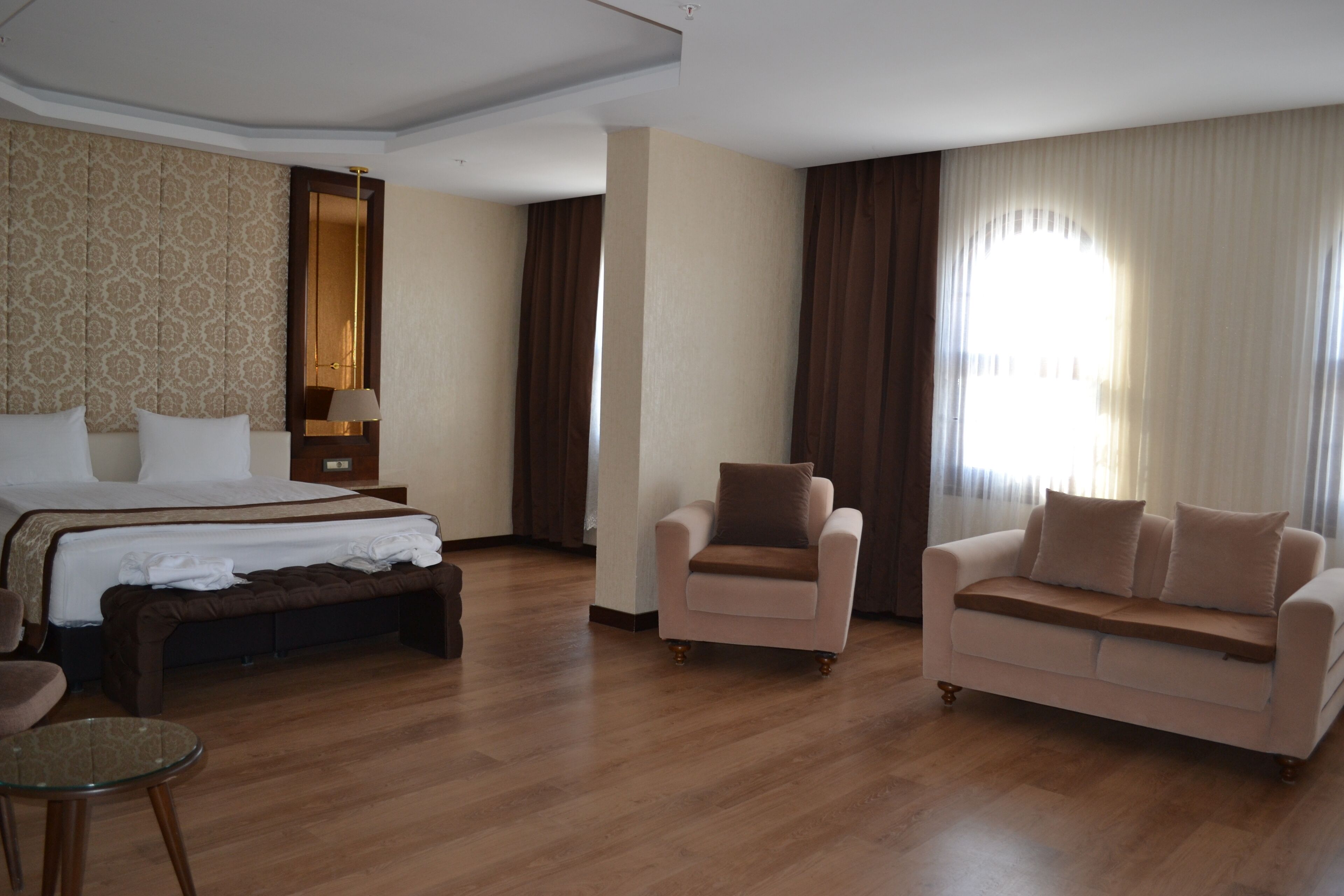 A hotel room with a large bed, a sofa, a chair, a small table, and a mirror.