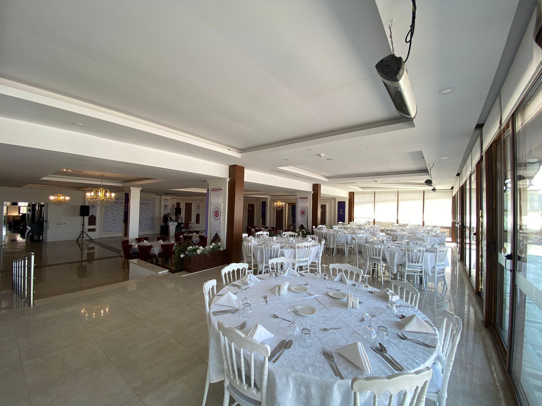 A spacious banquet hall with round tables set for dining, large windows, and a high ceiling.