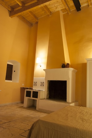 Una habitación con chimenea, una cama, una mesita y una lámpara fijada a la pared.
