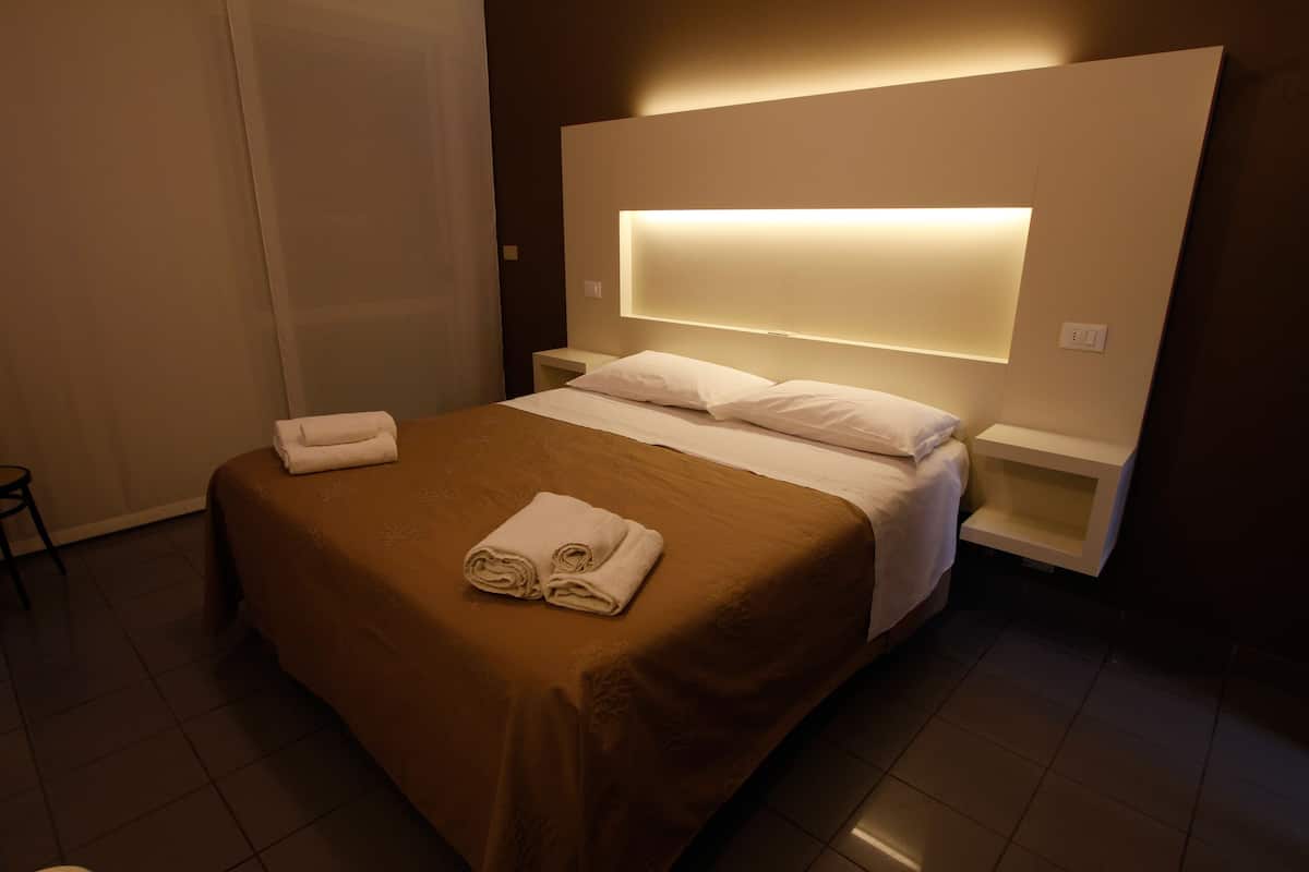 Une chambre d’hôtel moderne avec un grand lit, une table de chevet et une tête de lit dotée d’un éclairage intégré.