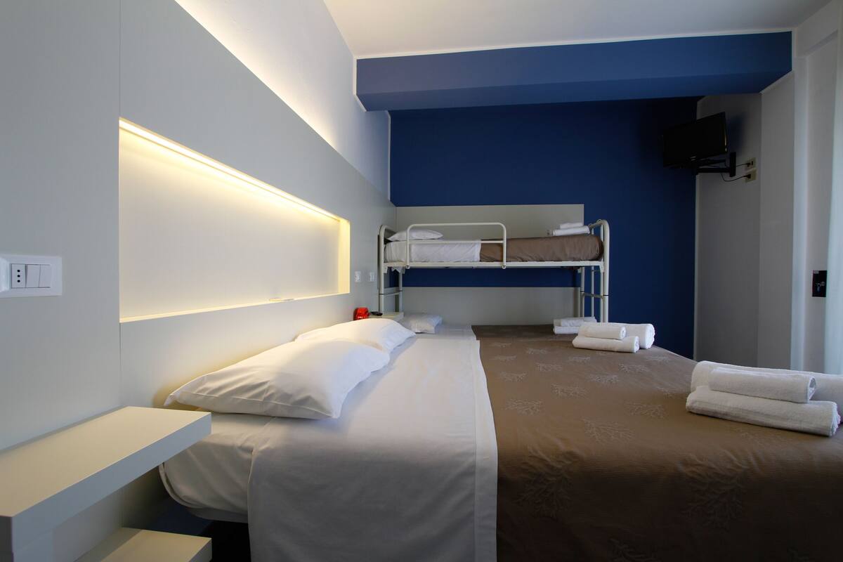 Une chambre d’hôtel avec un lit superposé, une table de chevet, un téléviseur fixé au mur et un espace douche.