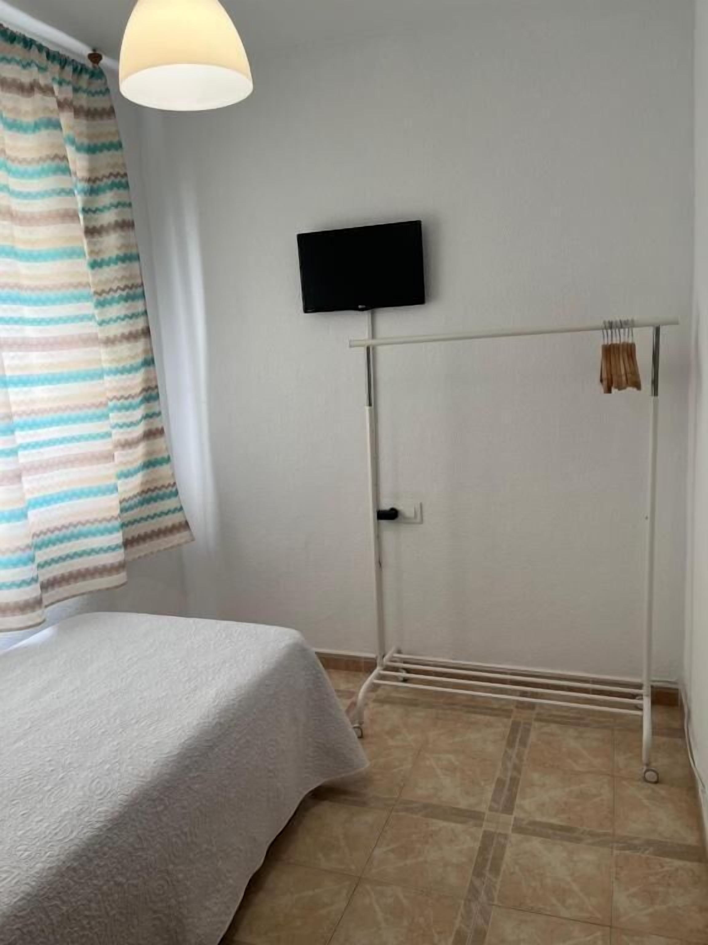 Une chambre avec un lit, un téléviseur fixé au mur, un radiateur et une fenêtre avec des rideaux.