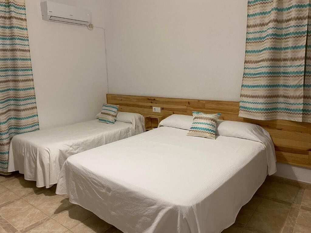 Una habitación de hotel con dos camas individuales, cabecero de madera y aire acondicionado instalado en la pared.