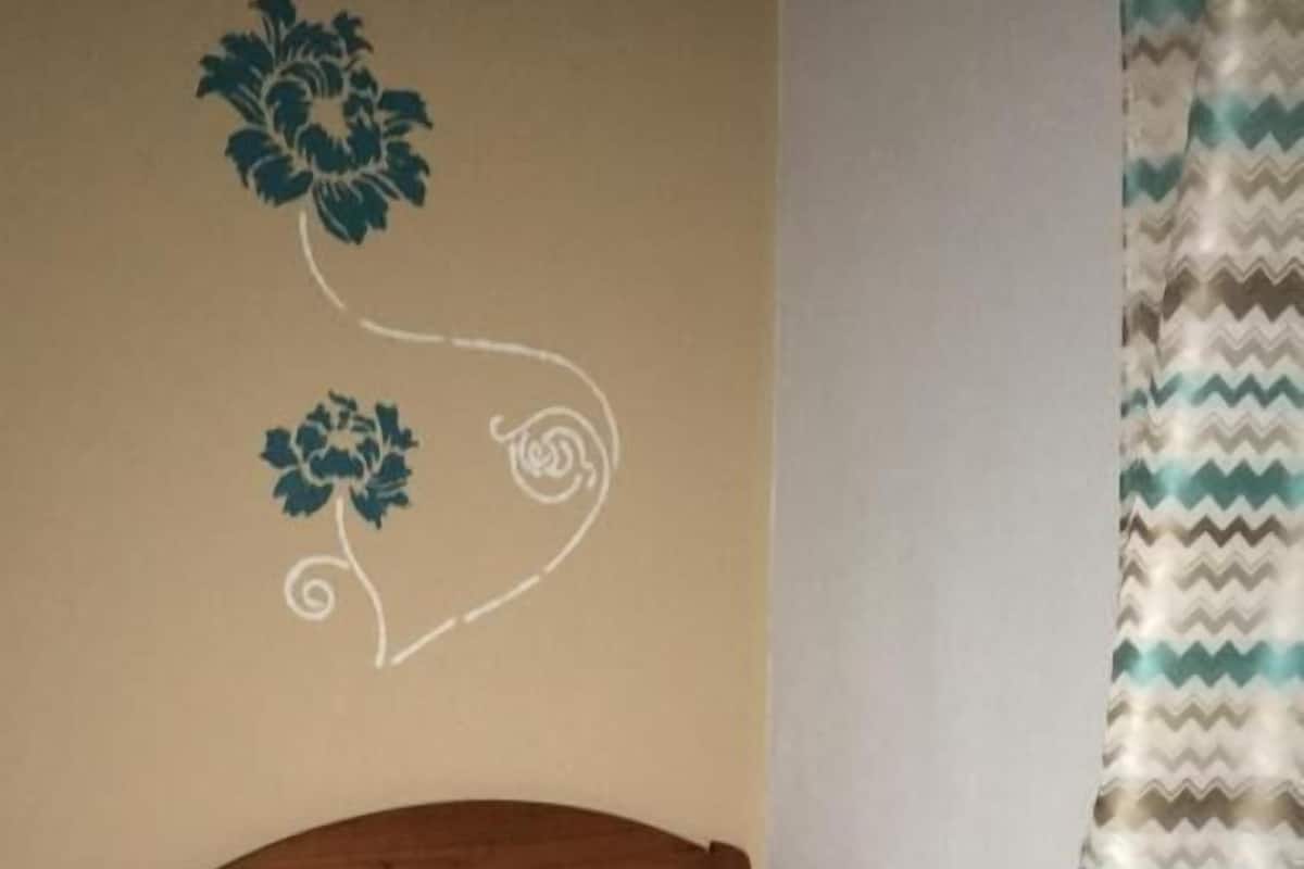 A bedroom with a wooden headboard, a bed with a patterned pillow, and a wall with a floral design.