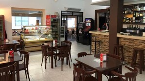 A restaurant with wooden tables and chairs, a glass display case with pastries, a jukebox, and a bar area with shelves of bottles.