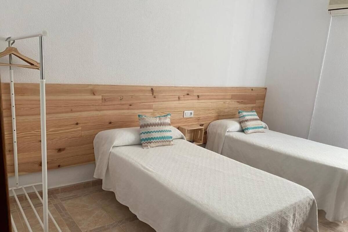 A room with two single beds, a wooden headboard, a white wall, and a metal rack.
