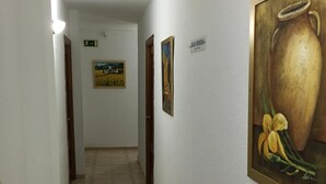 A hallway with tiled flooring, white walls, and framed artwork including a painting of a vase with flowers.