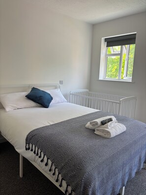 Ein Hotelzimmer mit einem Bett, weißer Bettwäsche, einer blau-weißen Decke und einem Fenster mit Blick auf Grünflächen.