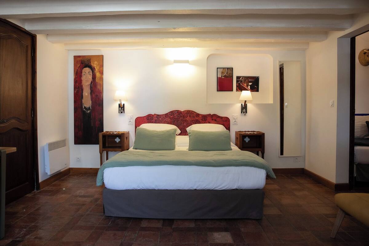 Een slaapkamer met een groot bed, twee nachtkastjes, een rood hoofdeinde en een schilderij aan de muur.