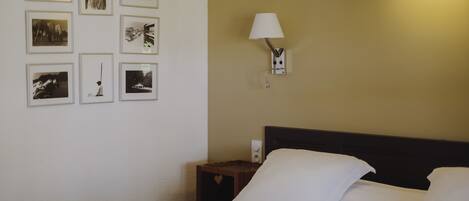 A hotel room with a neatly made bed, a nightstand with a lamp, and a wall adorned with framed photographs.