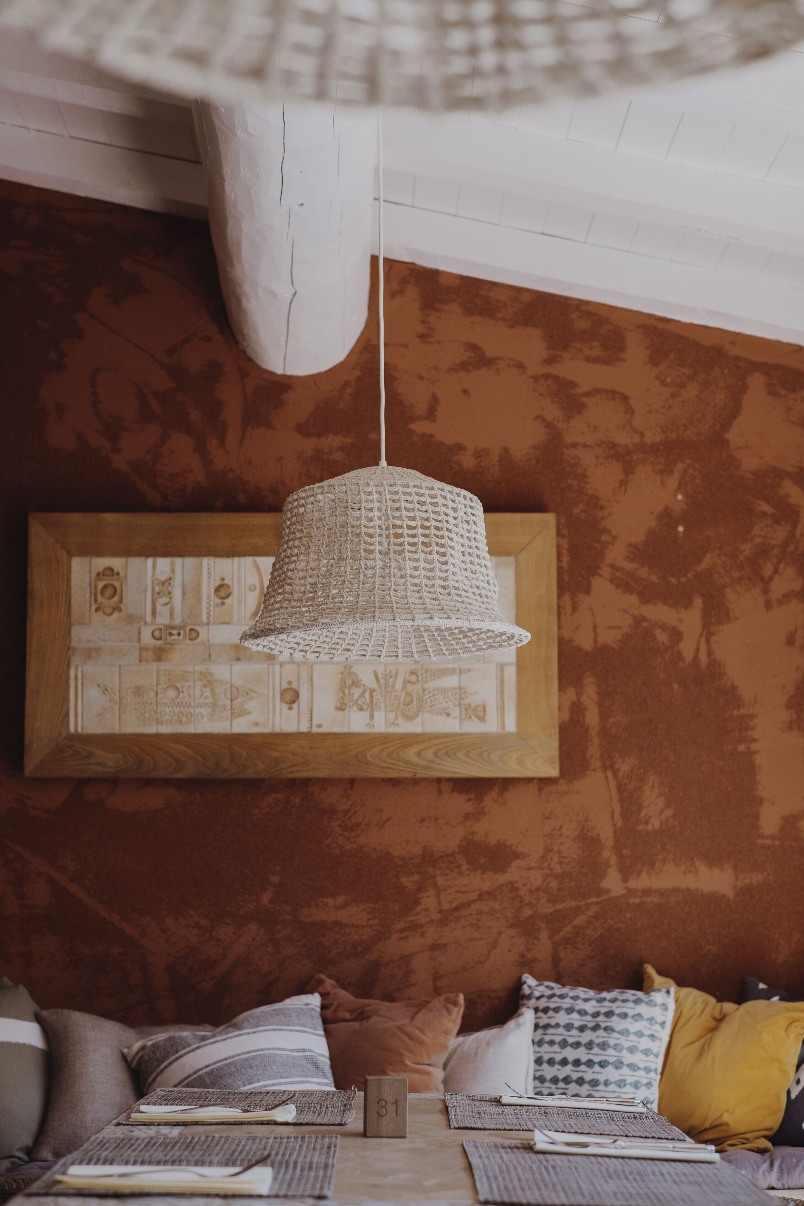 A cozy room with a woven pendant light, a patterned wall, and a bed with various pillows.