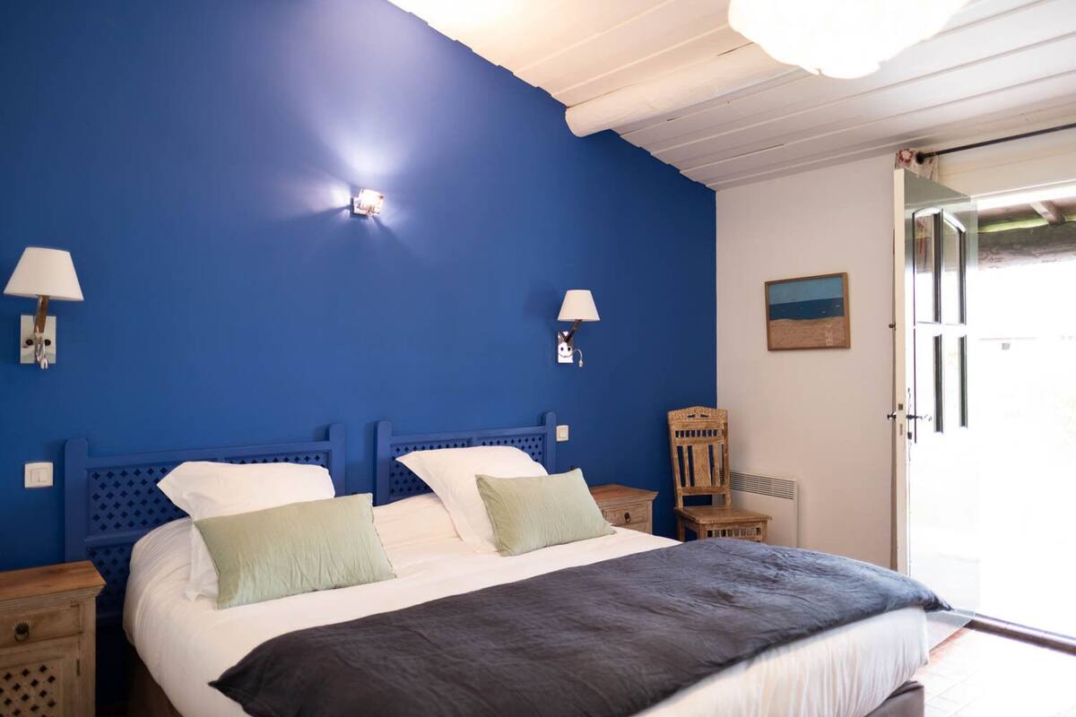 Een slaapkamer met een groot bed, twee nachtkastjes, een houten stoel en een schilderij aan de muur.