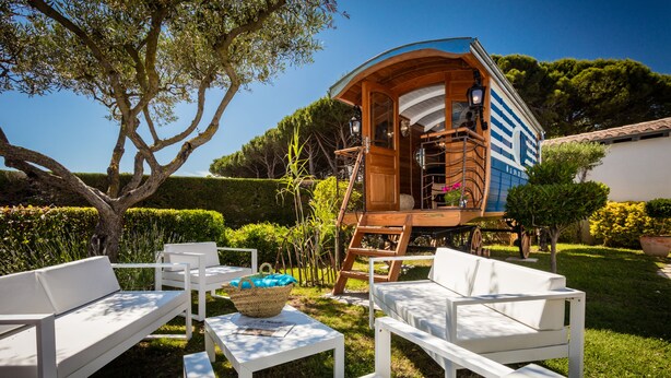 Une cabane en bois dotée d’un balcon, entourée de meubles d’extérieur blancs et d’un jardin bien entretenu.
