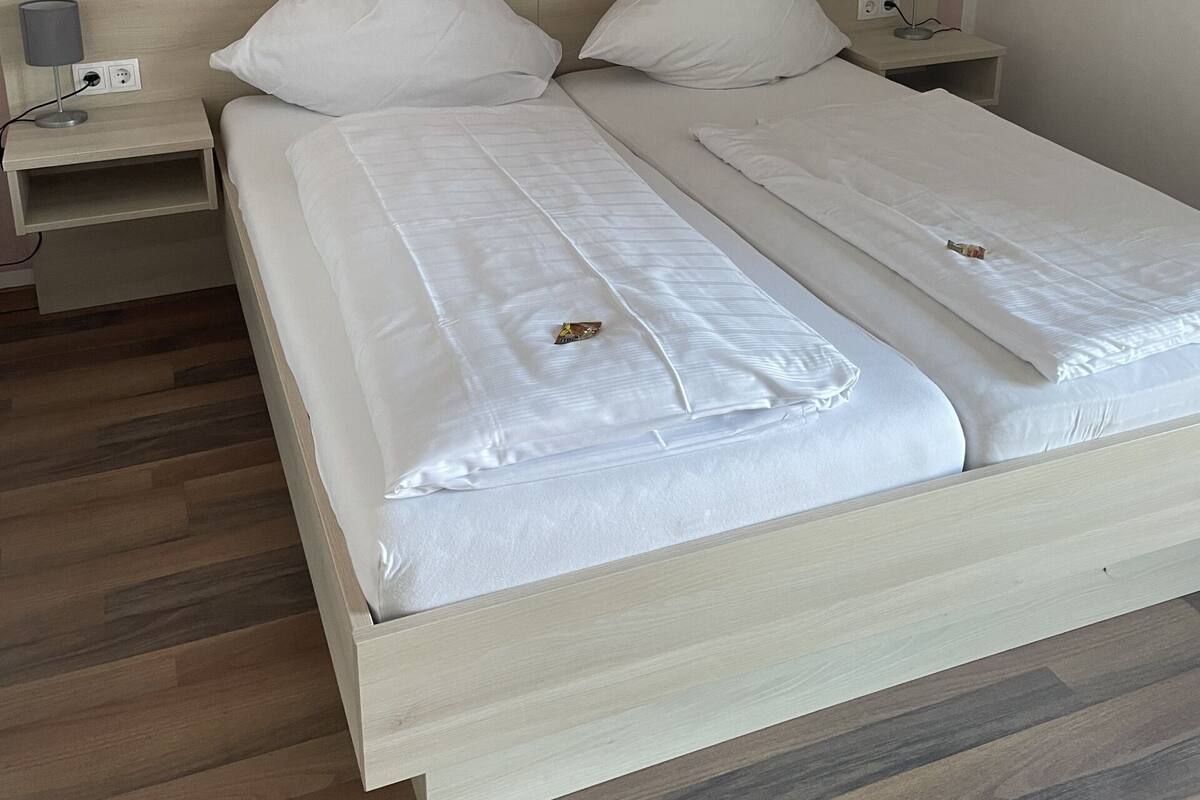 Una cama doble con ropa blanca, dos mesitas de noche con lámparas y un cabecero de madera.
