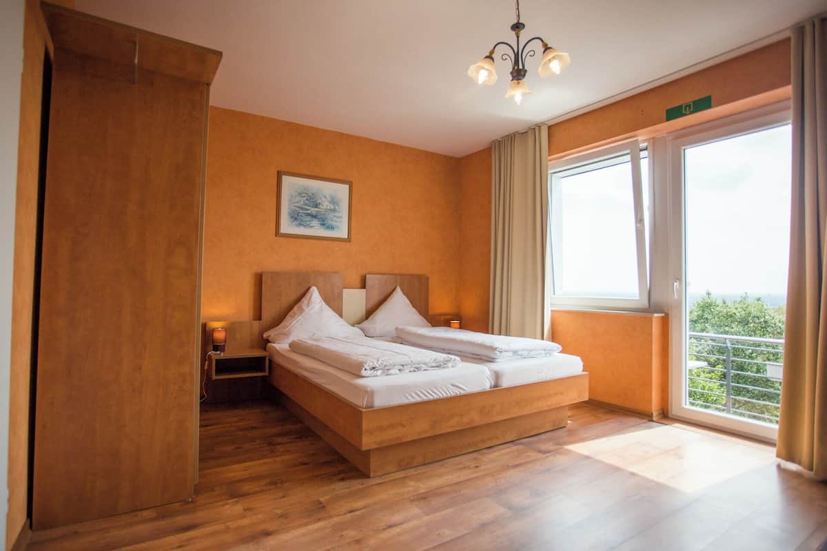Habitación de hotel con cama de madera, mesita de noche, un cuadro y un balcón con vistas.