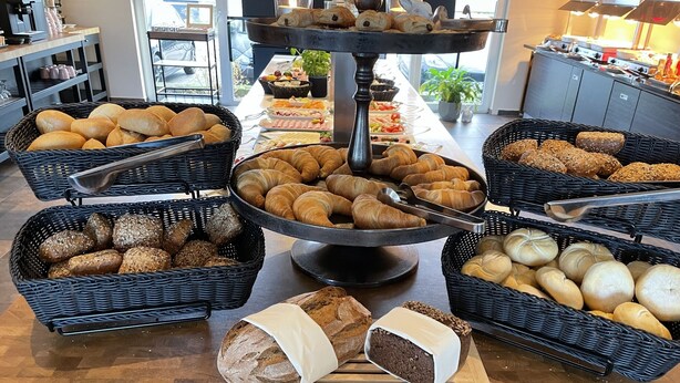 A buffet with various breads, pastries, and a cake on a wooden table. - Hotel Bismarckhöhe (Tecklenburg)