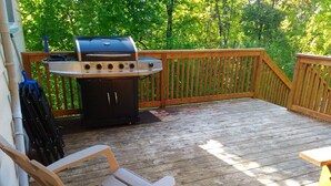 A wooden deck with a grill, a chair, and a table. - The Oak Cottage At Shiloh Cottages - Fenelon Falls, Ontario (Fenelon Falls, Ontario)