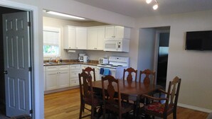 A compact kitchen with white cabinets, a microwave, stove, and a dining table with wooden chairs. - The Oak Cottage At Shiloh Cottages - Fenelon Falls, Ontario (Fenelon Falls, Ontario)