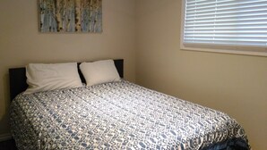 A bedroom with a bed, two pillows, a window with blinds, and a wall-mounted abstract art piece. - The Oak Cottage At Shiloh Cottages - Fenelon Falls, Ontario (Fenelon Falls, Ontario)