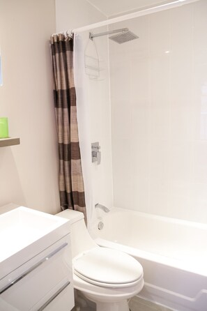 Un baño con inodoro blanco, bañera y ducha con cortina marrón y blanca.