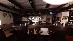 A bar area with wooden stools, a bar counter, and shelves stocked with bottles and glasses. - Landhaus Sundern (Tecklenburg)