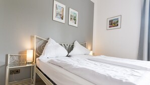 A neatly made bed with white linens, a bedside table with a lamp, and two framed pictures on the wall. - Landhaus Sundern (Tecklenburg)