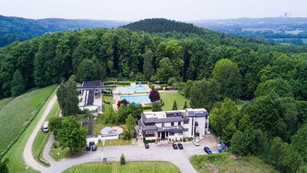 A hotel with a swimming pool, surrounded by lush greenery and hills. - Landhaus Sundern (Tecklenburg)