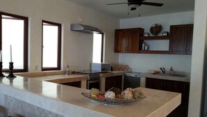 A modern kitchen with a central island, built-in oven, microwave, and dishwasher. There are wooden cabinets and a ceiling fan. -  CASA MONARCA. Self sustained house in La Ropa, Zihuatanejo, Gro. México. (Zihuatanejo)