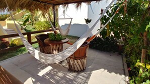 A hammock under a thatched roof, a wooden table with bananas, and a view of a garden with plants and a building in the background. -  CASA MONARCA. Self sustained house in La Ropa, Zihuatanejo, Gro. México. (Zihuatanejo)