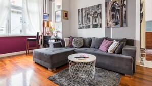 A modern living room with a grey sectional sofa, a round coffee table, and a large window with curtains. - UNIQUE & URBAN 4* House DelMarco apt @ TOP CENTRAL LOCATION (Split)