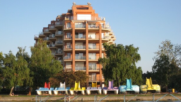 Un edificio de varios pisos con balcones, vista al frente marítimo y muelles flotantes de colores.