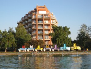 A multi-story building with balconies, a waterfront, and colorful floating docks. - Galerius Panoráma Beach - C Apartman (Siófok)