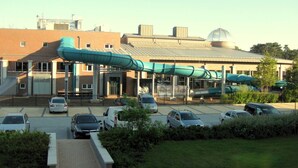 Un edificio con una zona exterior techada, estacionamiento y paisaje verde.